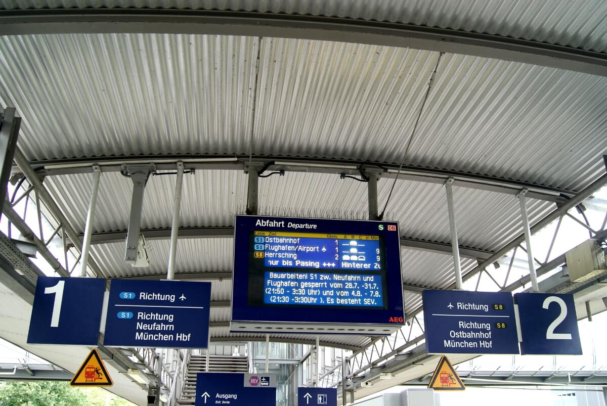 Zwischen den Gleisen 1 und 2 hängt eine Anzeigetafel, auf der die Abfahrtszeiten der Züge angezeigt wird.